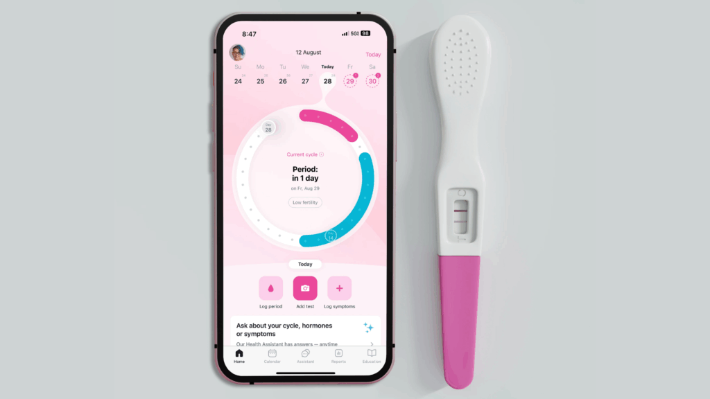 Celular exibindo aplicativo de ciclo menstrual ao lado de um teste de gravidez digital, representando o uso da tecnologia no acompanhamento da fertilidade feminina.