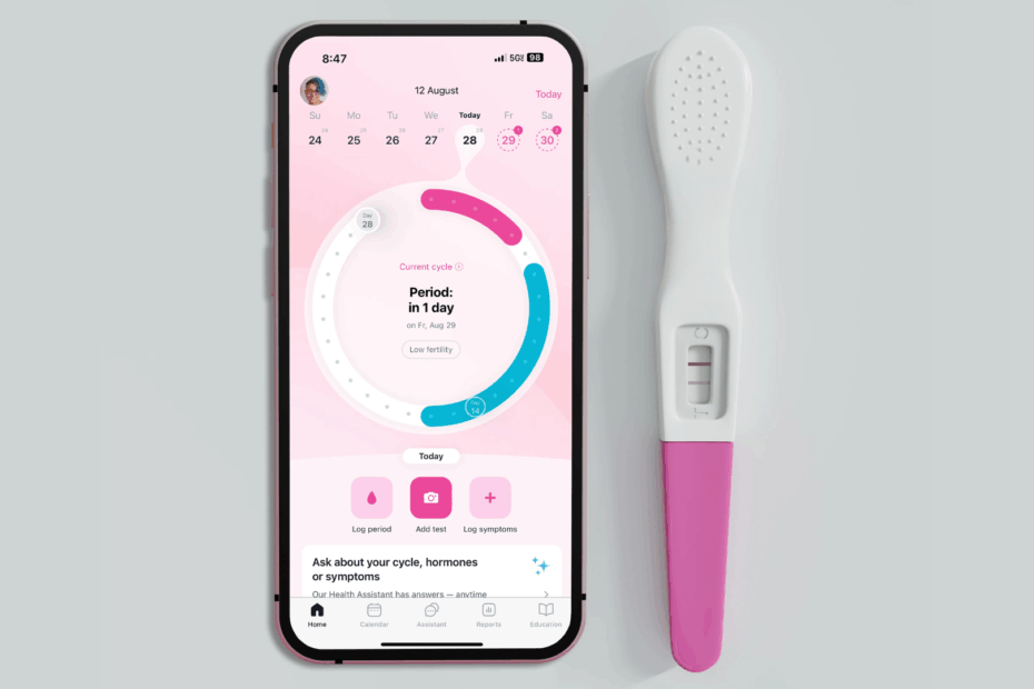 Celular exibindo aplicativo de ciclo menstrual ao lado de um teste de gravidez digital, representando o uso da tecnologia no acompanhamento da fertilidade feminina.