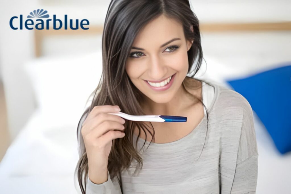 Mulher sorrindo enquanto segura um teste de gravidez Clearblue, representando o monitoramento online dos sintomas da gravidez de forma prática e confiável
