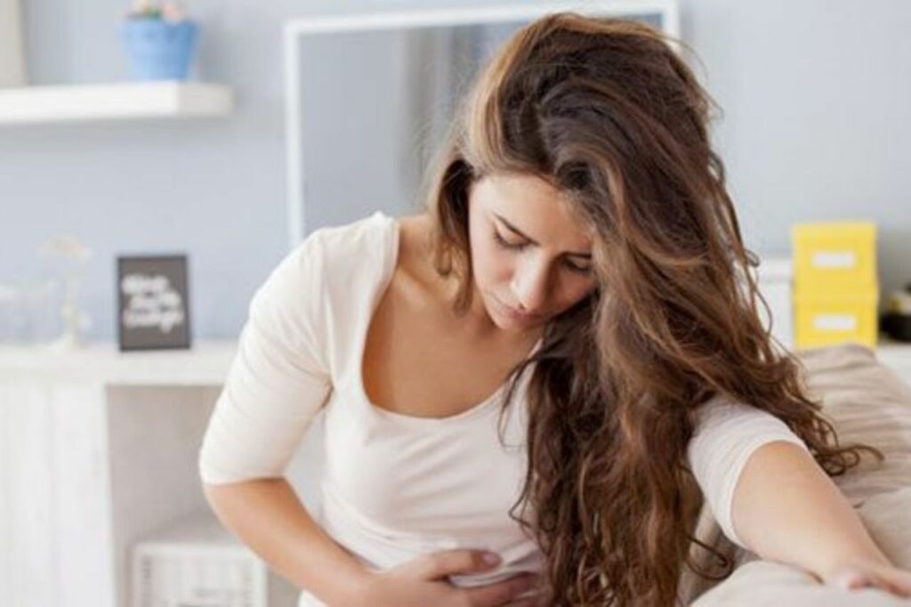 Mulher com a mão no abdômen sentindo desconforto, representando um dos primeiros sinais de gravidez comuns nas primeiras semanas.