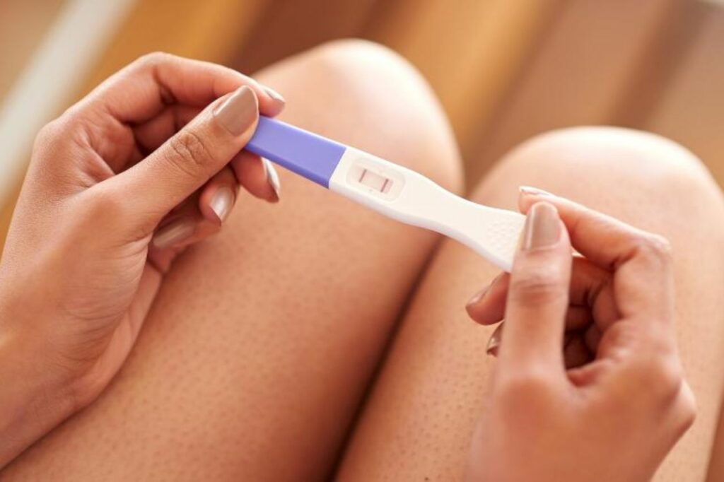 Pessoa segurando um teste de gravidez positivo, representando os primeiros sinais de gravidez e a confirmação inicial da gestação.